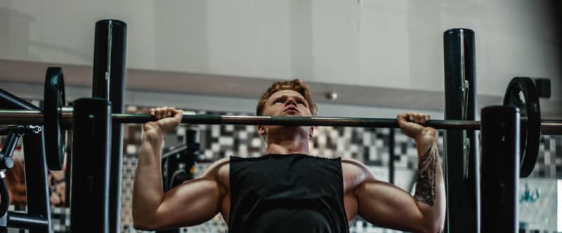 Image d'un homme musculeux à la salle de sport en train de soulever une altère sur un banc de pousse.