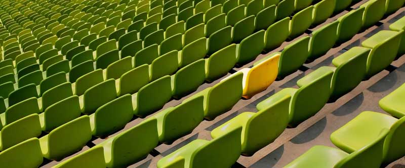 rangées de chaises vertes dans un stade, une seule chaise est jaune au milieu.