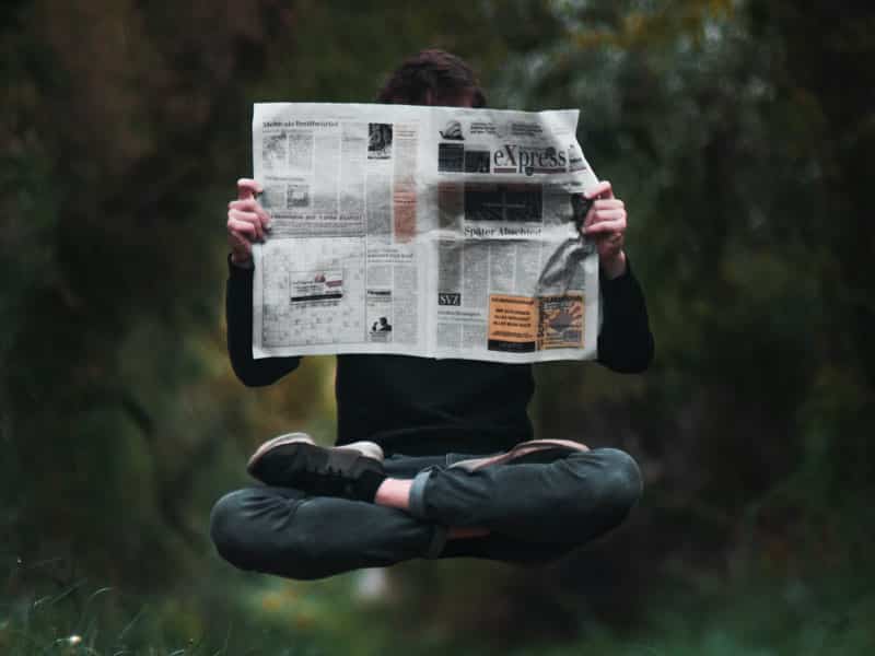 Homme en lévitation en train de lire des articles de journal, les pieds croisés en position du lotus